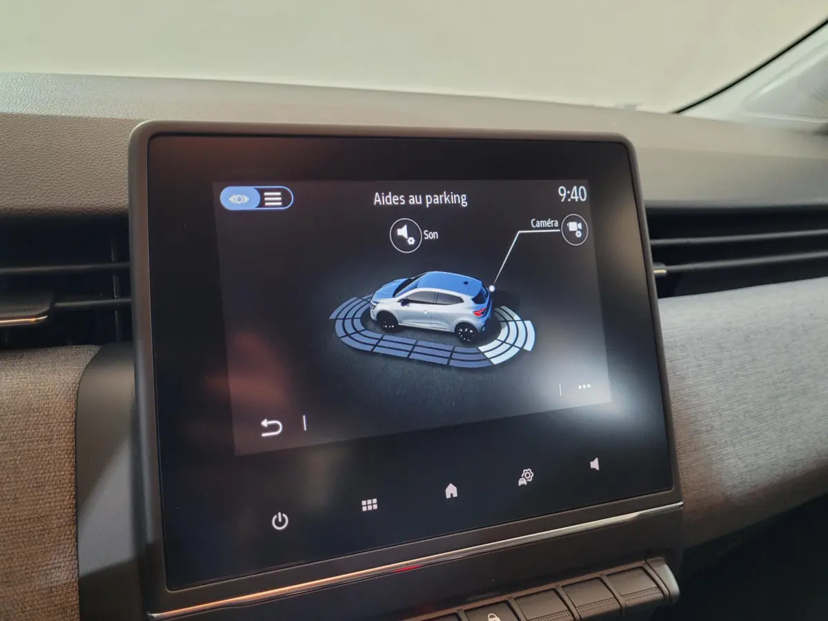 Écran tactile central affichant l'aide au parking avec vue 3D d'une Renault Clio bleue dans l'habitacle.