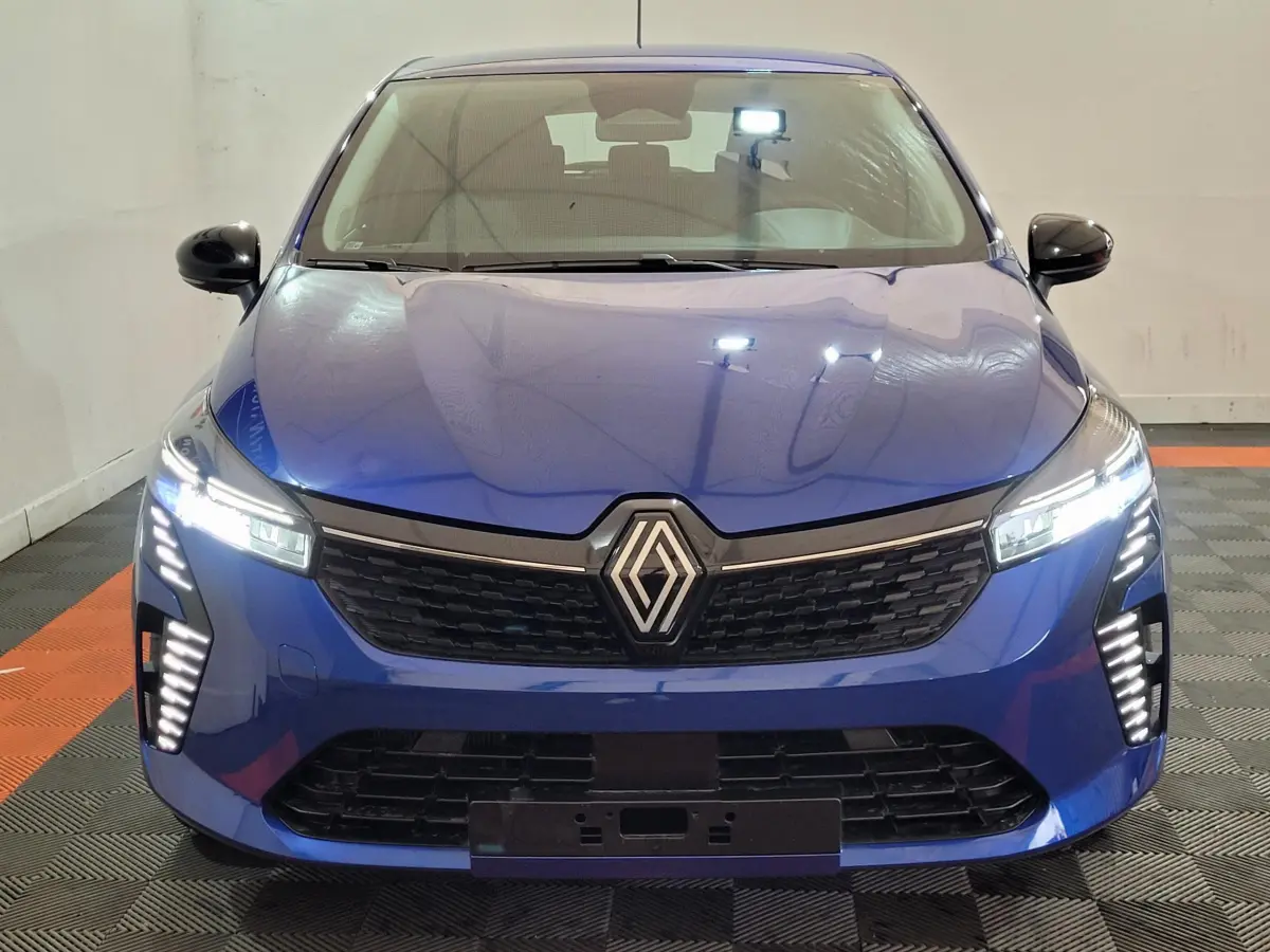 Vue frontale d'une Renault Clio Evolution Blue dCi 100 2025 bleu avec phares et feux LED allumés dans un intérieur neutre.