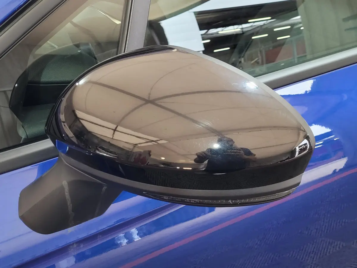 Rétroviseur côté gauche noir brillant sur Renault Clio bleu, avec reflet de l'environnement intérieur visible.