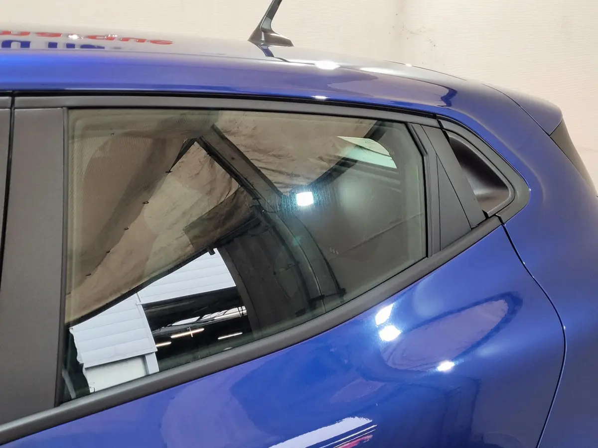 Vue côté gauche arrière d'une Renault Clio bleu brillant, mettant en valeur la ligne fluide et la vitre latérale arrière.