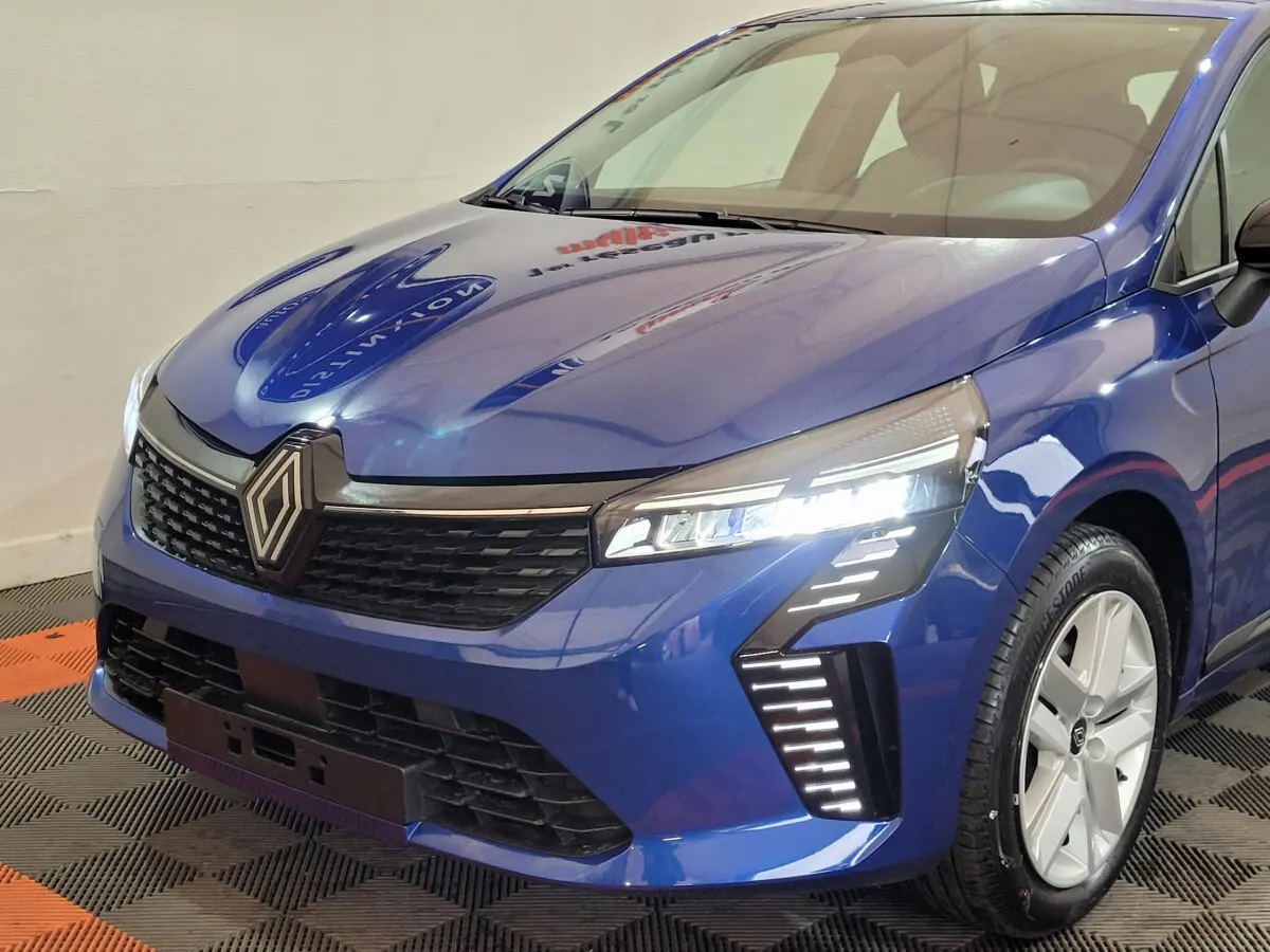 Vue 3/4 avant droite d'une Renault Clio bleu avec phares LED et calandre noire distinctive.