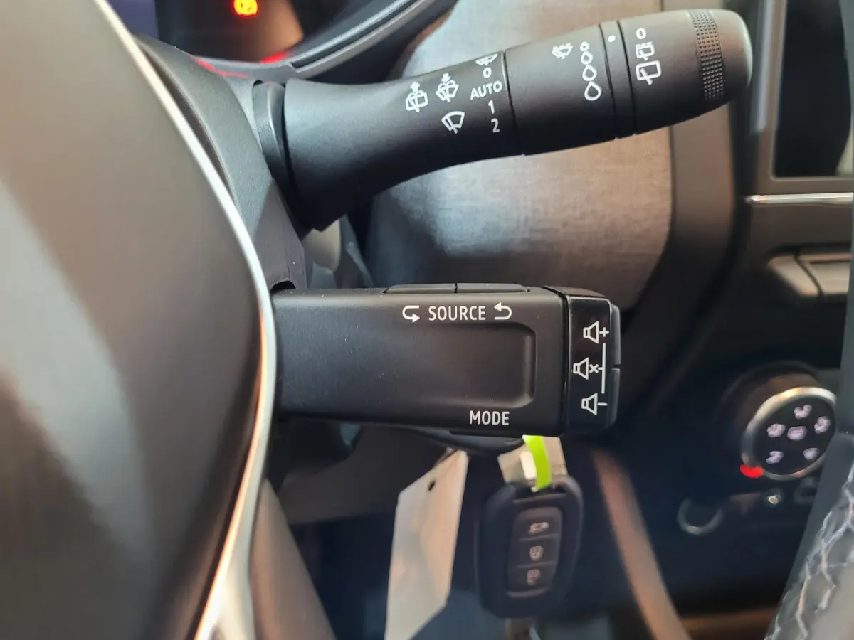 Gros plan sur la commande multifonctions à gauche du volant de la Renault Clio bleu, avec touches source et mode visibles.