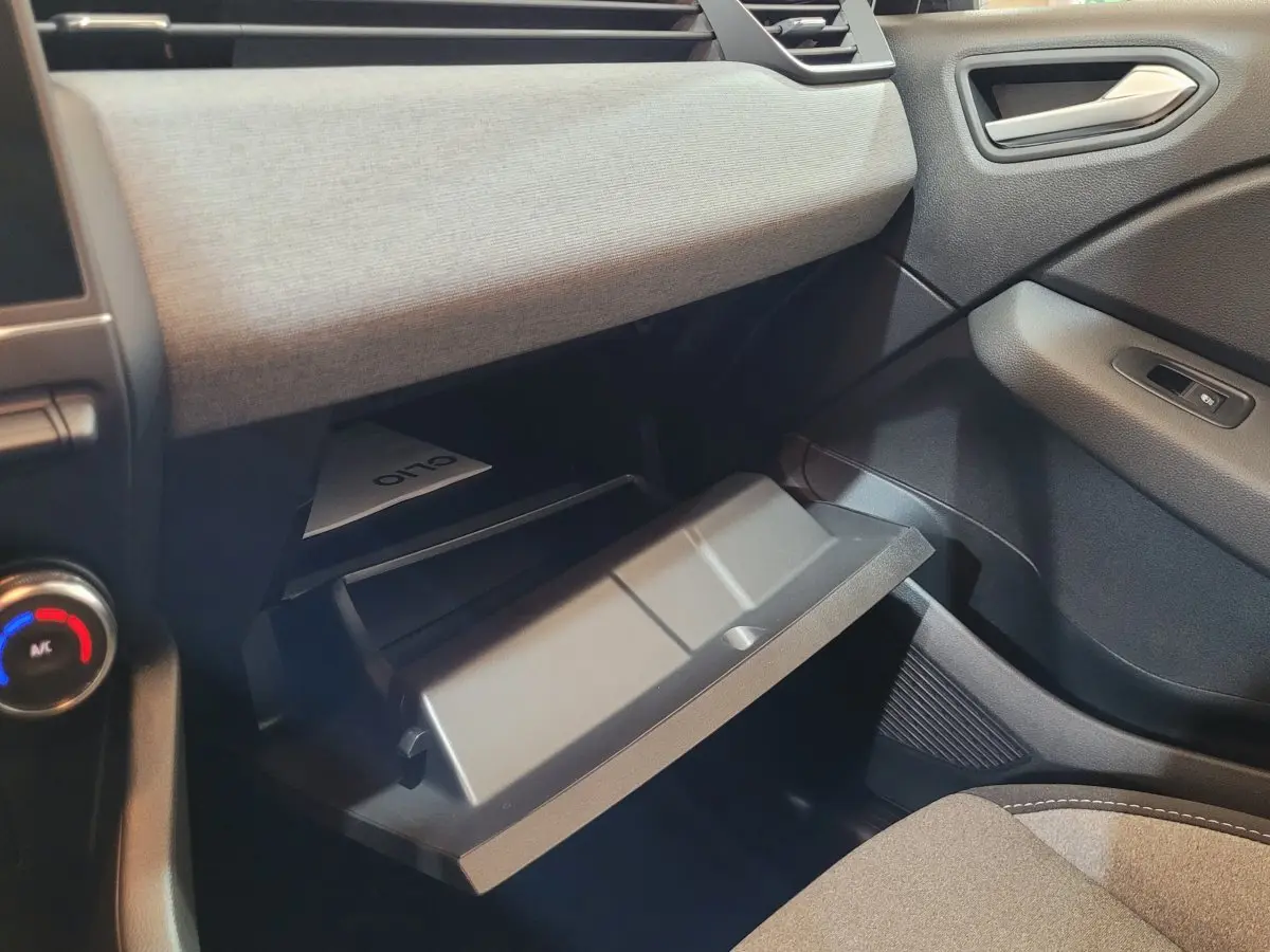 Intérieur de la Renault Clio 2025 bleu, vue côté passager sur la boîte à gants ouverte et tableau de bord gris clair.
