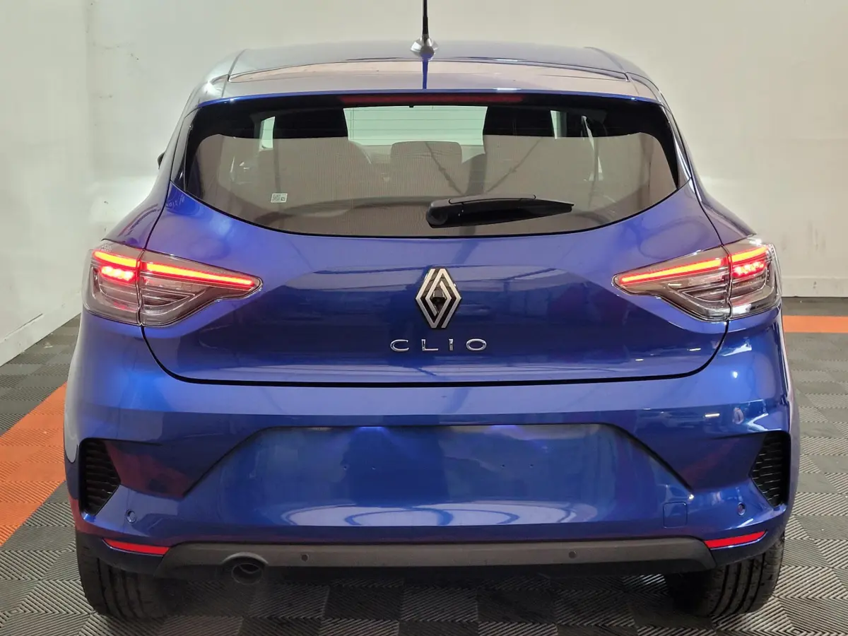 Vue arrière d'une Renault Clio bleu électrique 2025 avec feux LED allumés et logo central visible.