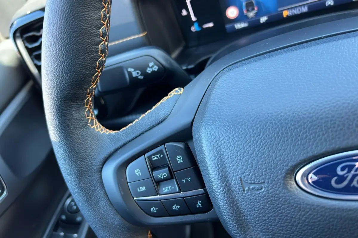 Gros plan sur le volant noir à surpiqûres orange du Ford Ranger 2025 avec commandes intégrées et logo Ford visible.