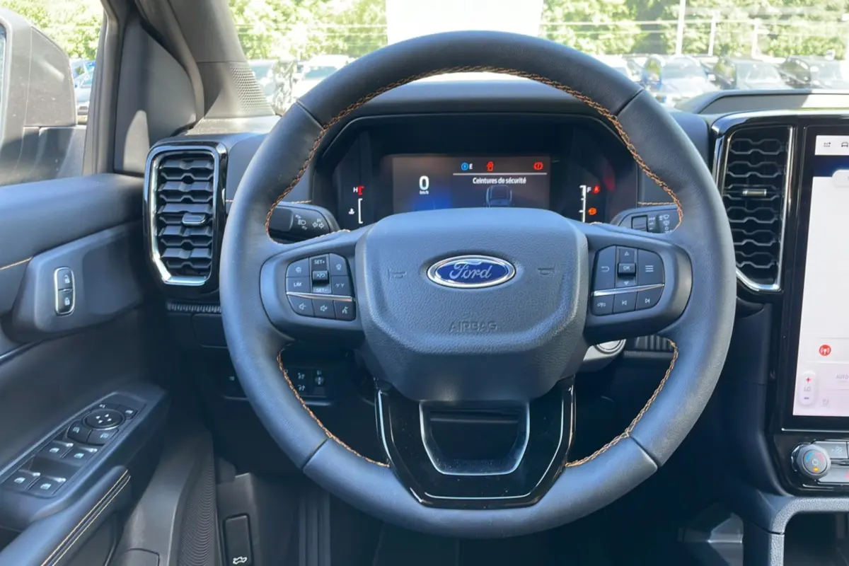 Vue intérieure centrée sur le volant du Ford Ranger 2025 gris carbone, avec commandes intégrées et tableau de bord digital.