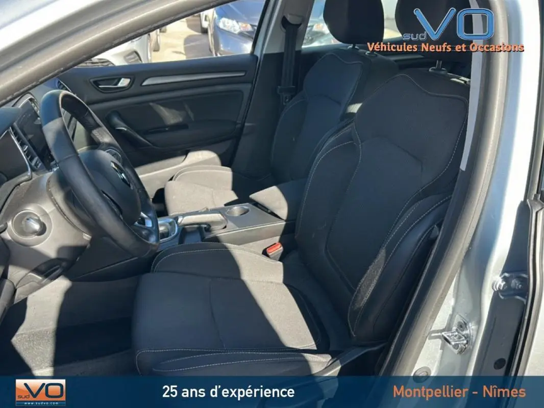 Vue intérieure côté conducteur de la Renault Mégane IV Berline gris clair, sièges noirs et tableau de bord visible.