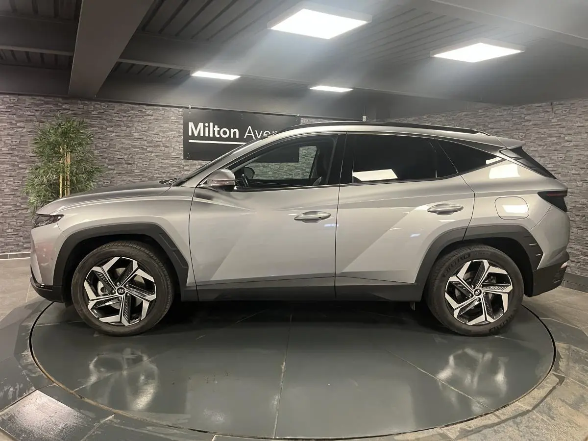 Vue de profil côté gauche du Hyundai Tucson gris métallisé 2023 avec jantes alliage et toit noir contrasté.