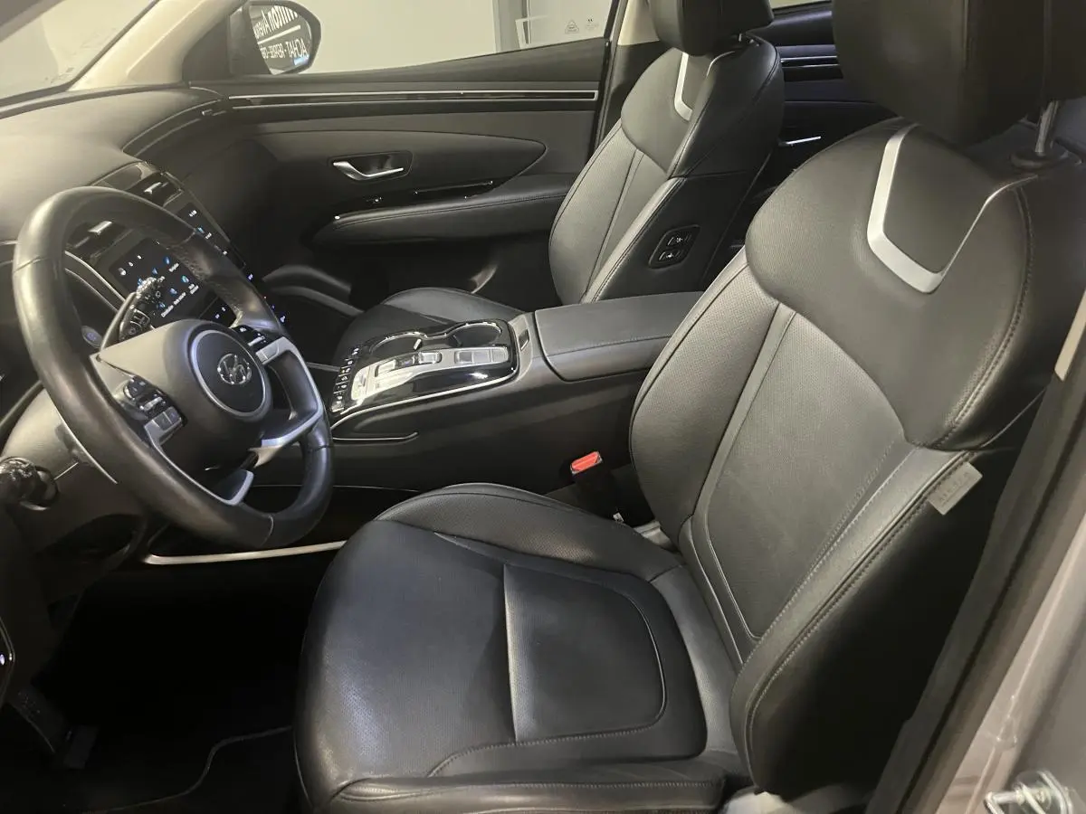 Intérieur du Hyundai Tucson 2023 vu côté conducteur, sièges cuir noirs et console centrale moderne avec commandes tactiles.