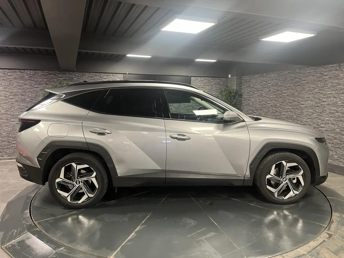 Profil droit du Hyundai Tucson 2023 gris métallisé avec jantes alliage et vitres surteintées en intérieur showroom.