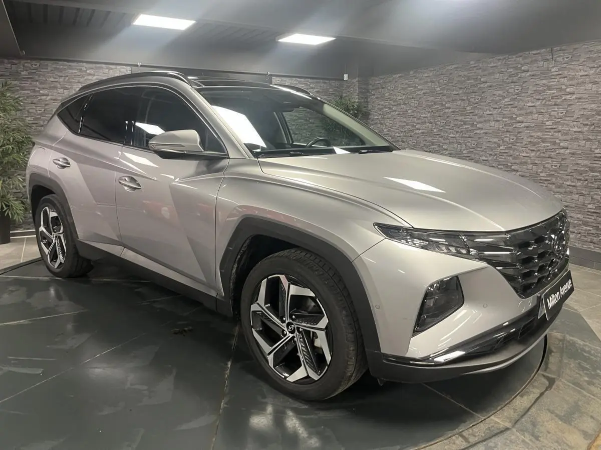 Vue 3/4 avant gauche d'un Hyundai Tucson gris métallisé avec calandre chromée et jantes alliage 19 pouces.