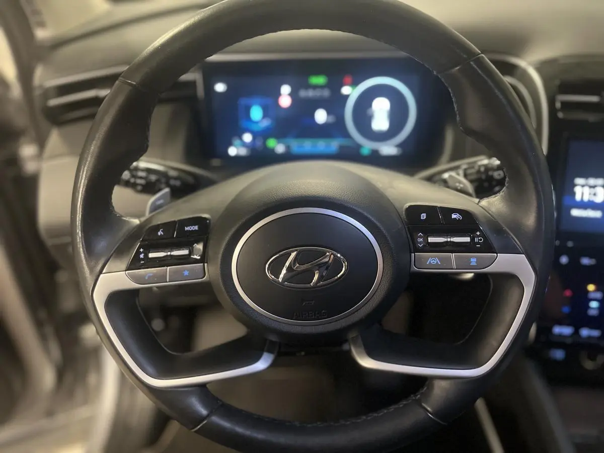 Vue rapprochée du volant cuir noir avec commandes intégrées du Hyundai Tucson gris 2023 hybride rechargeable.