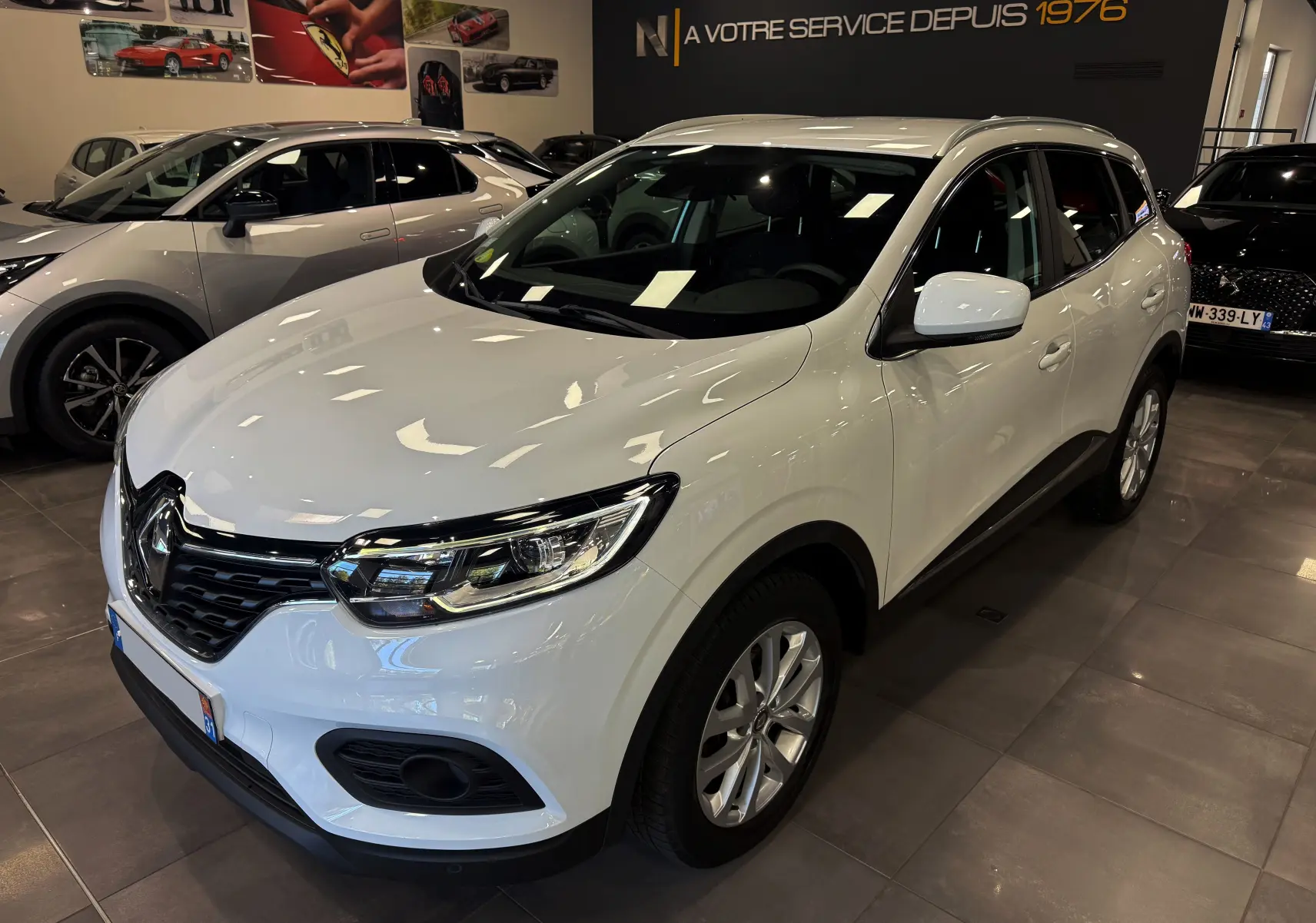 Renault Kadjar Blanc Glacier en 3/4 avant droit dans un showroom avec reflets lumineux sur la carrosserie.