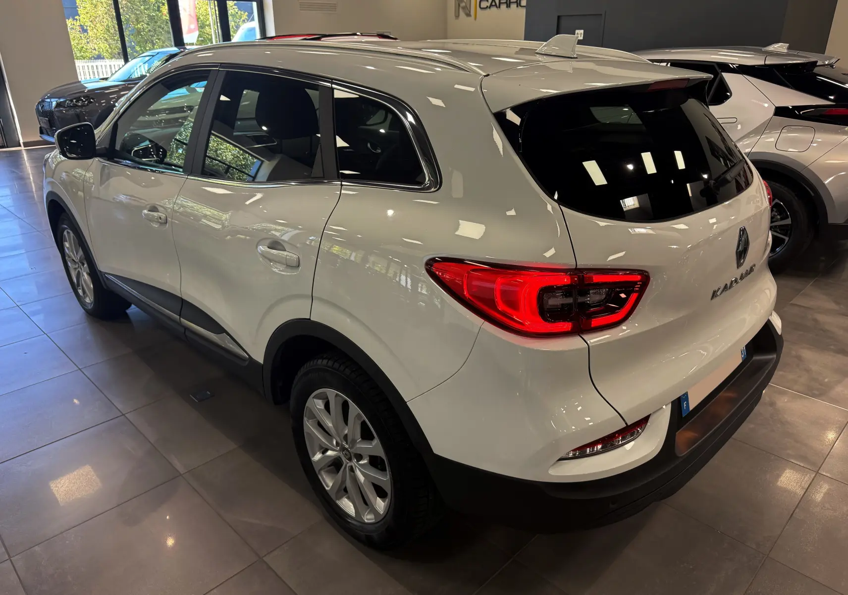 Vue 3/4 arrière droite d'un Renault Kadjar Blanc Glacier 2020 en showroom, avec feux arrière allumés et jantes alliage.
