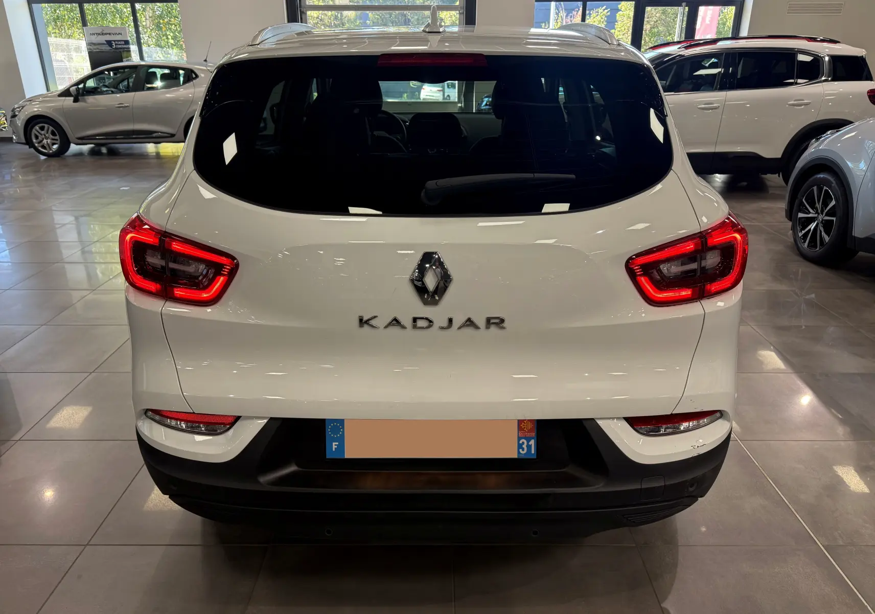 Vue arrière d'un Renault Kadjar blanc Glacier de 2020 avec feux arrière allumés dans un showroom.