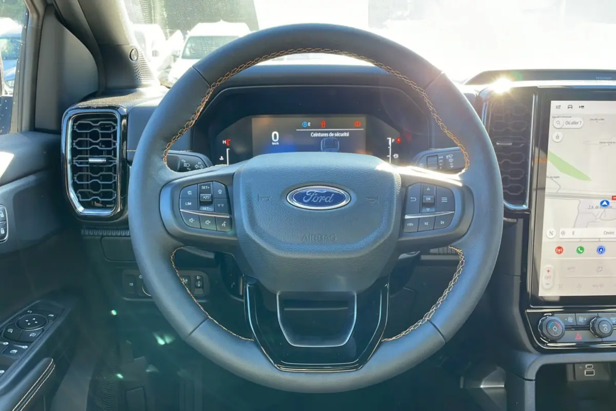 Vue intérieure centrée sur le volant du Ford Ranger 2025 gris iconic, avec tableau de bord numérique et écran tactile visible.