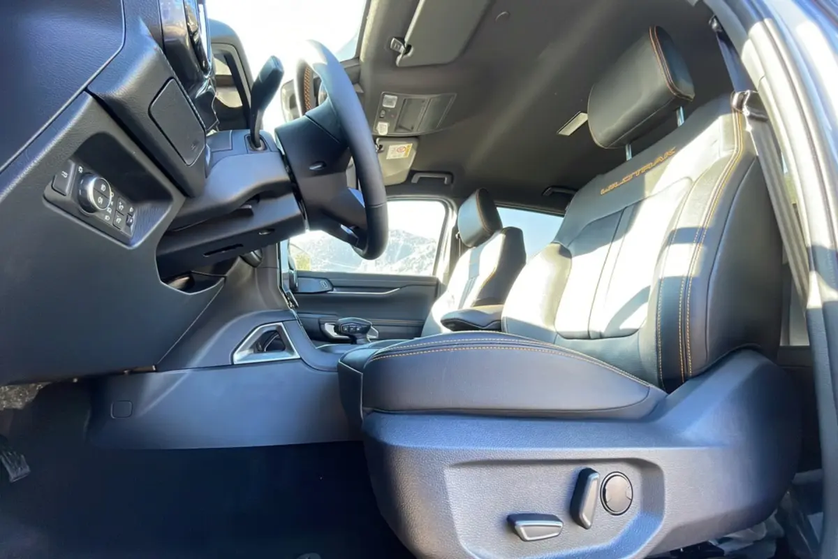 Intérieur du Ford Ranger 2025 Wildtrak Plus, vue côté conducteur sur les sièges noirs avec surpiqûres orange et volant.
