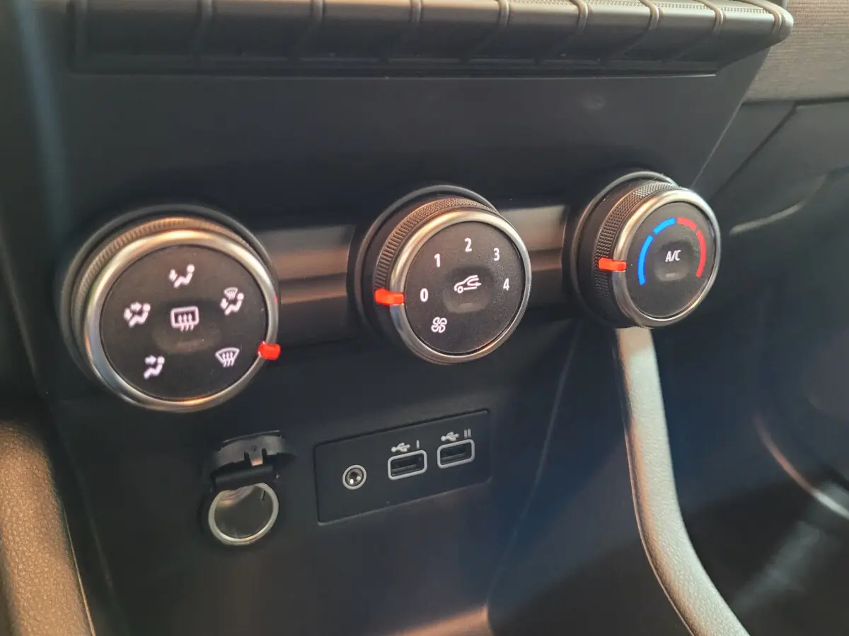 Gros plan sur les commandes de climatisation et ports USB du tableau de bord de la Renault Clio gris foncé.