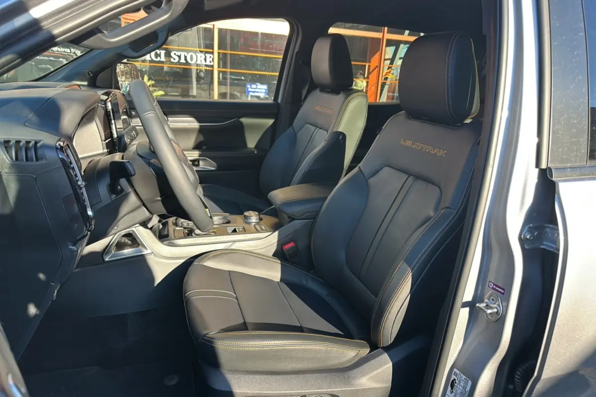 Vue intérieure côté conducteur du Ford Ranger 2025 gris iconic, sièges en cuir avec logo Wildtrak brodé et surpiqûres orange.