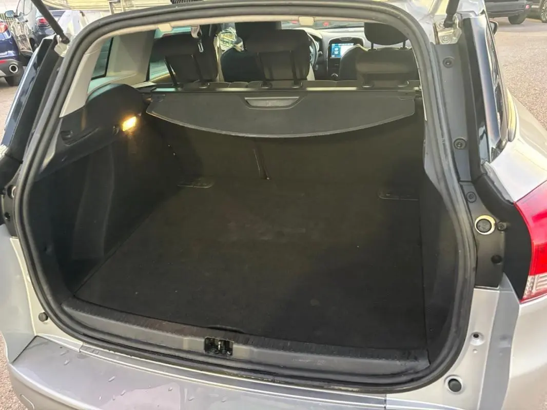 Coffre ouvert vu de l'arrière d'une Renault Clio IV Estate gris clair, montrant l'espace de chargement et la plage arrière.