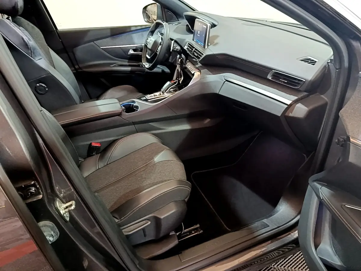 Vue intérieure côté passager avant du Peugeot 3008 gris foncé, avec tableau de bord moderne et sièges en cuir noir.