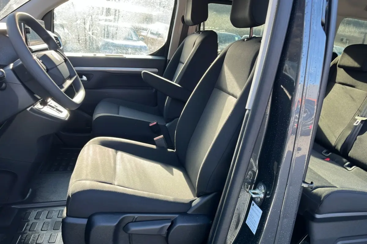 Vue intérieure côté conducteur du Peugeot Traveller gris titane 2025, montrant les sièges avant avec accoudoir central et volant multifonctions.