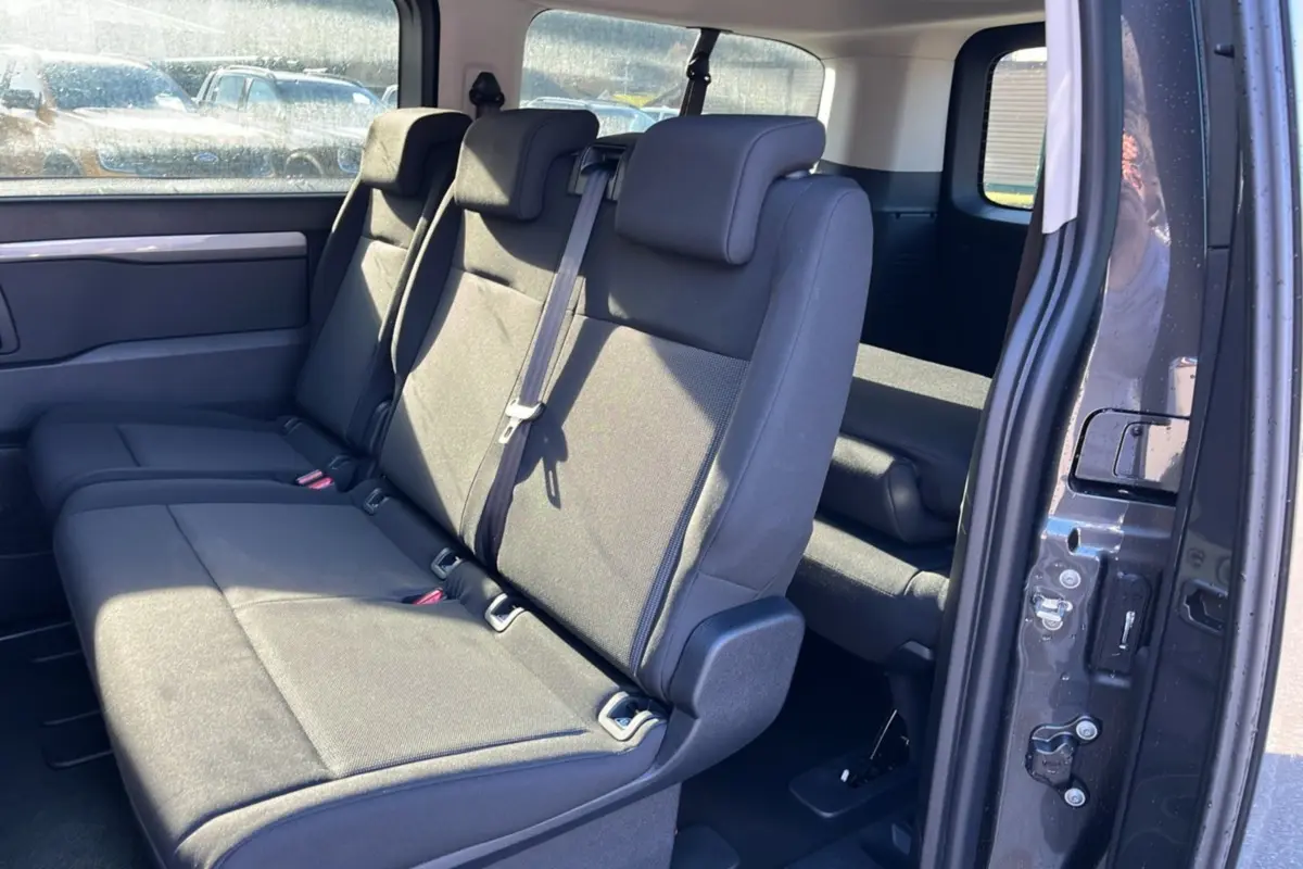 Vue intérieure côté droit sur la banquette arrière noire du Peugeot Traveller gris titane avec porte coulissante ouverte.