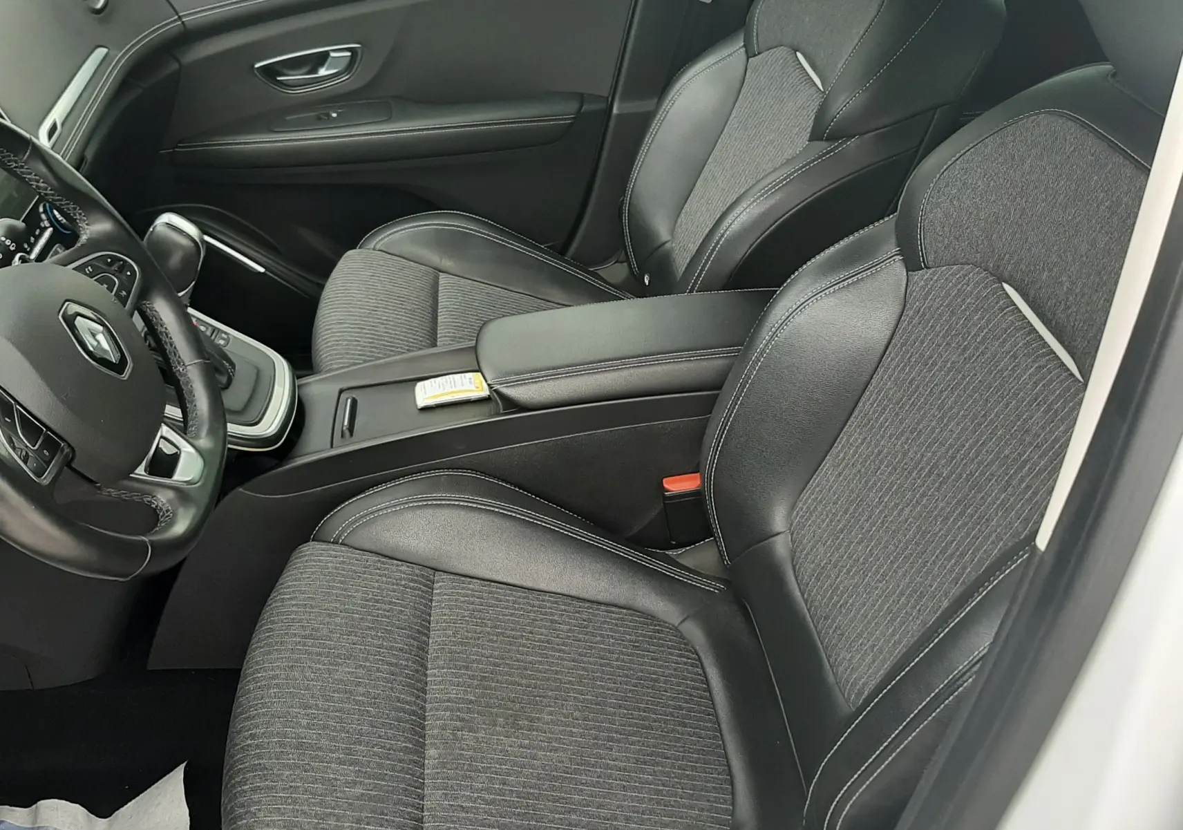 Vue intérieure côté conducteur du Renault Scénic IV 1.3 TCE 140 Intens avec sièges tissu et cuir noir, volant multifonction et console centrale.
