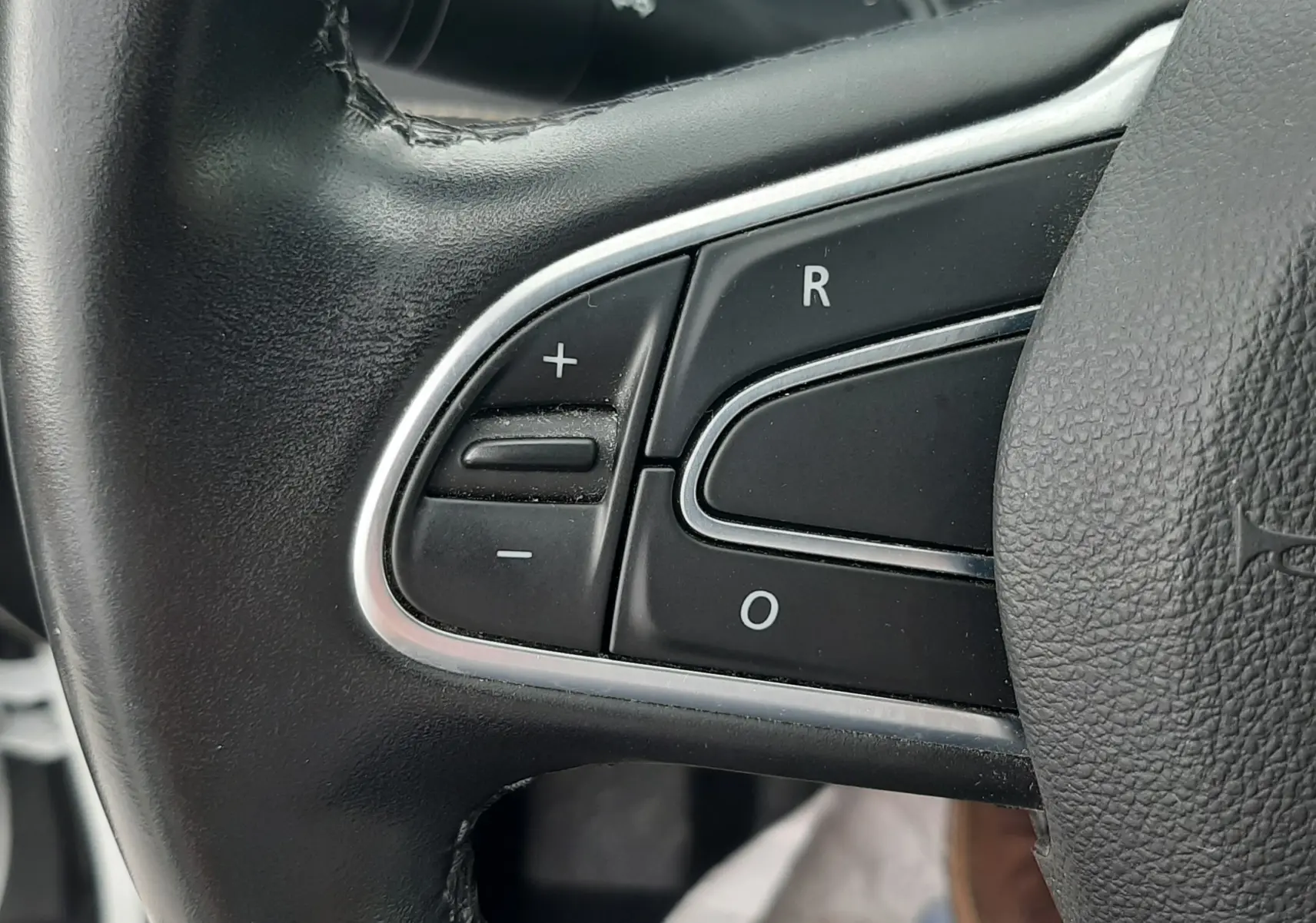 Gros plan sur les commandes gauche du volant noir du Renault Scénic IV blanc nacré, boutons de régulateur de vitesse visibles.