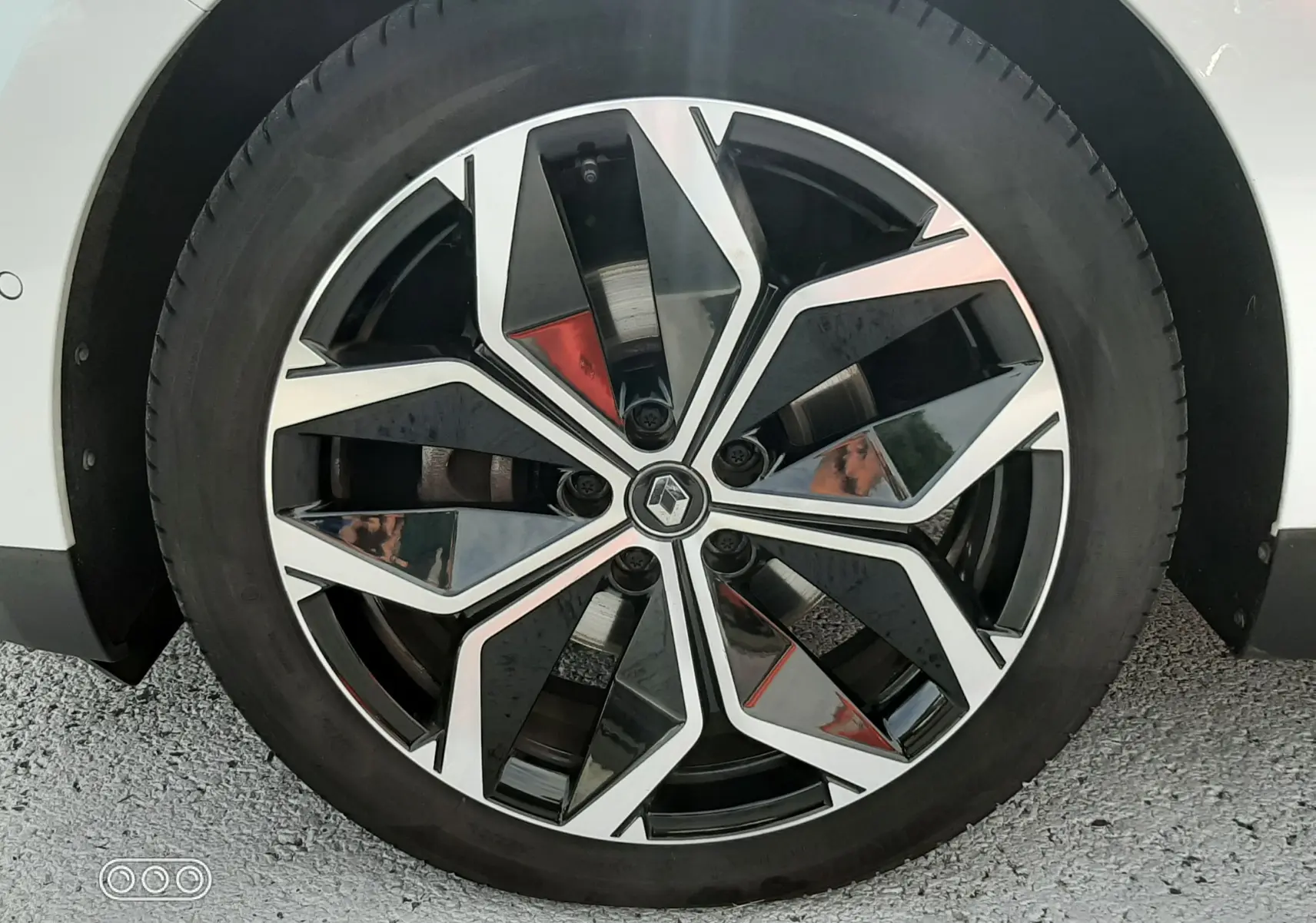 Gros plan sur la roue avant droite du Renault Scénic IV blanc nacré avec jante alliage diamantée noire et argent.