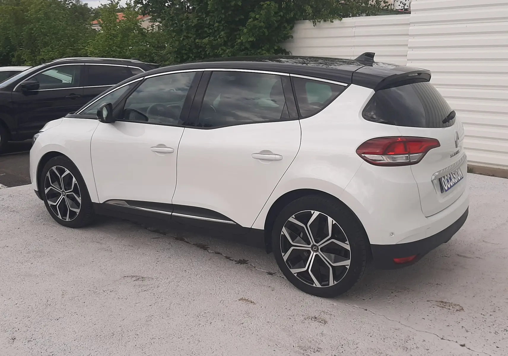 Renault Scénic IV blanc nacré avec toit noir, vue 3/4 arrière droit, jantes alliage distinctives, stationné en extérieur.