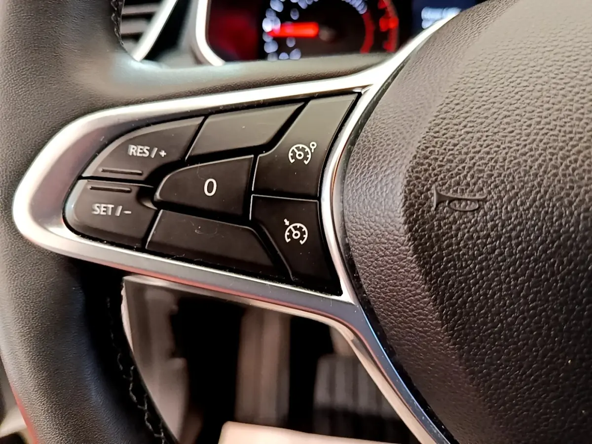 Gros plan sur les commandes de régulateur de vitesse à gauche du volant noir d'une Renault Clio Business Blue dCi 85 blanche.