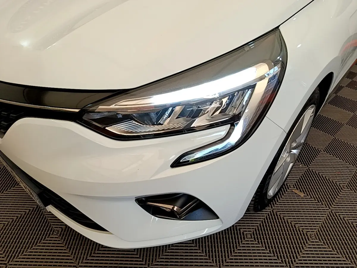 Gros plan sur l'avant droit blanc d'une Renault Clio 2020, mettant en valeur le phare LED et la jante alliage.