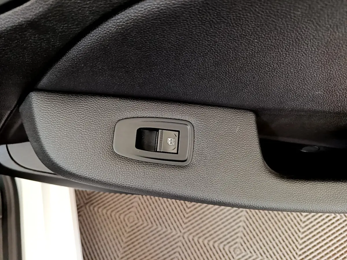 Gros plan sur le bouton de commande de la vitre électrique côté conducteur d’une Renault Clio Business Blue dCi blanche.