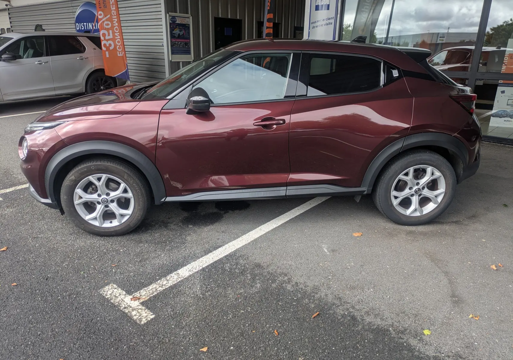 Vue de profil côté gauche d'un Nissan Juke rouge 2020, soulignant ses jantes alliage et ses protections noires sur les passages de roue.