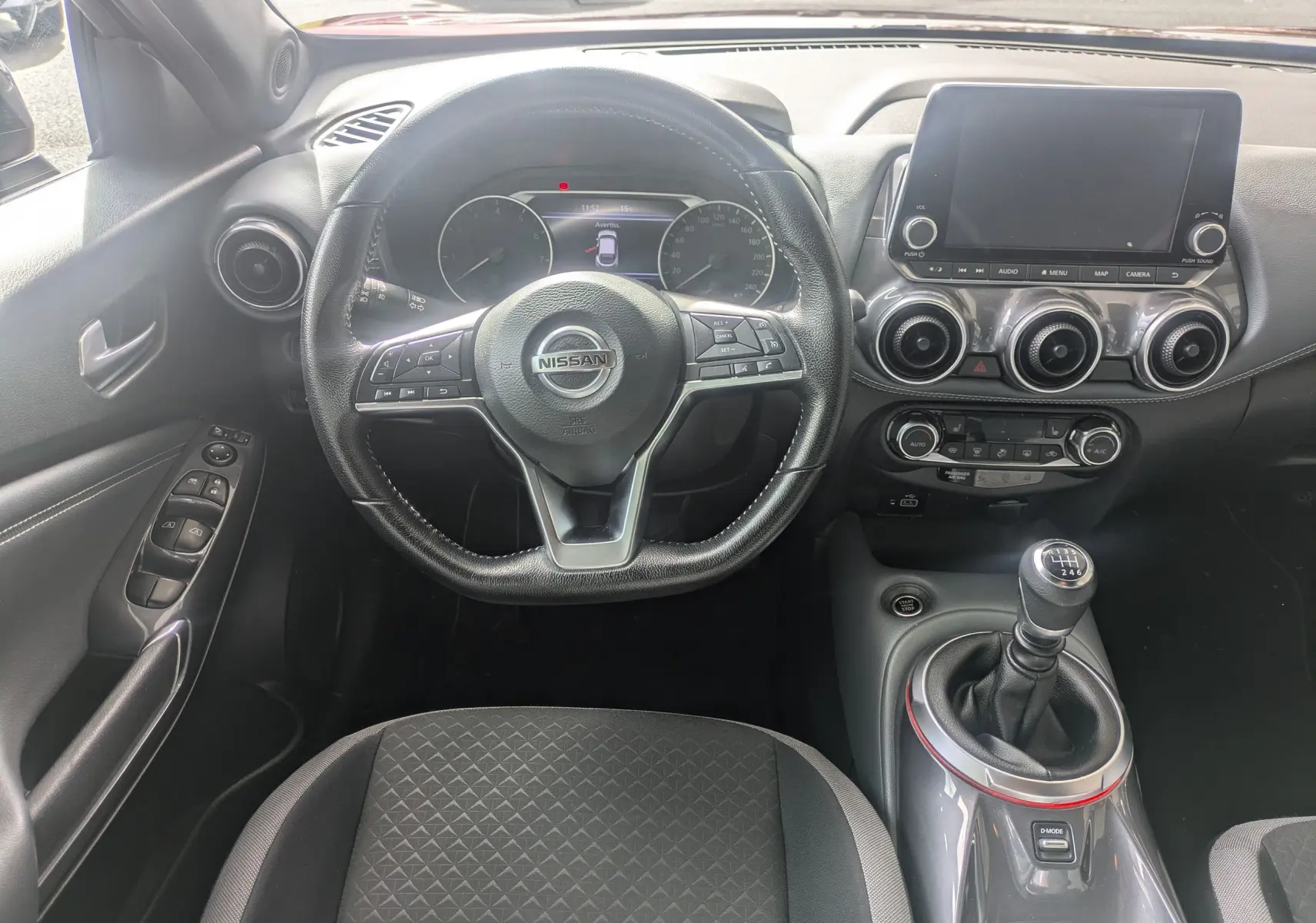 Vue intérieure centrée sur le volant et la console du Nissan Juke 2020, avec levier de vitesse manuel et écran tactile.