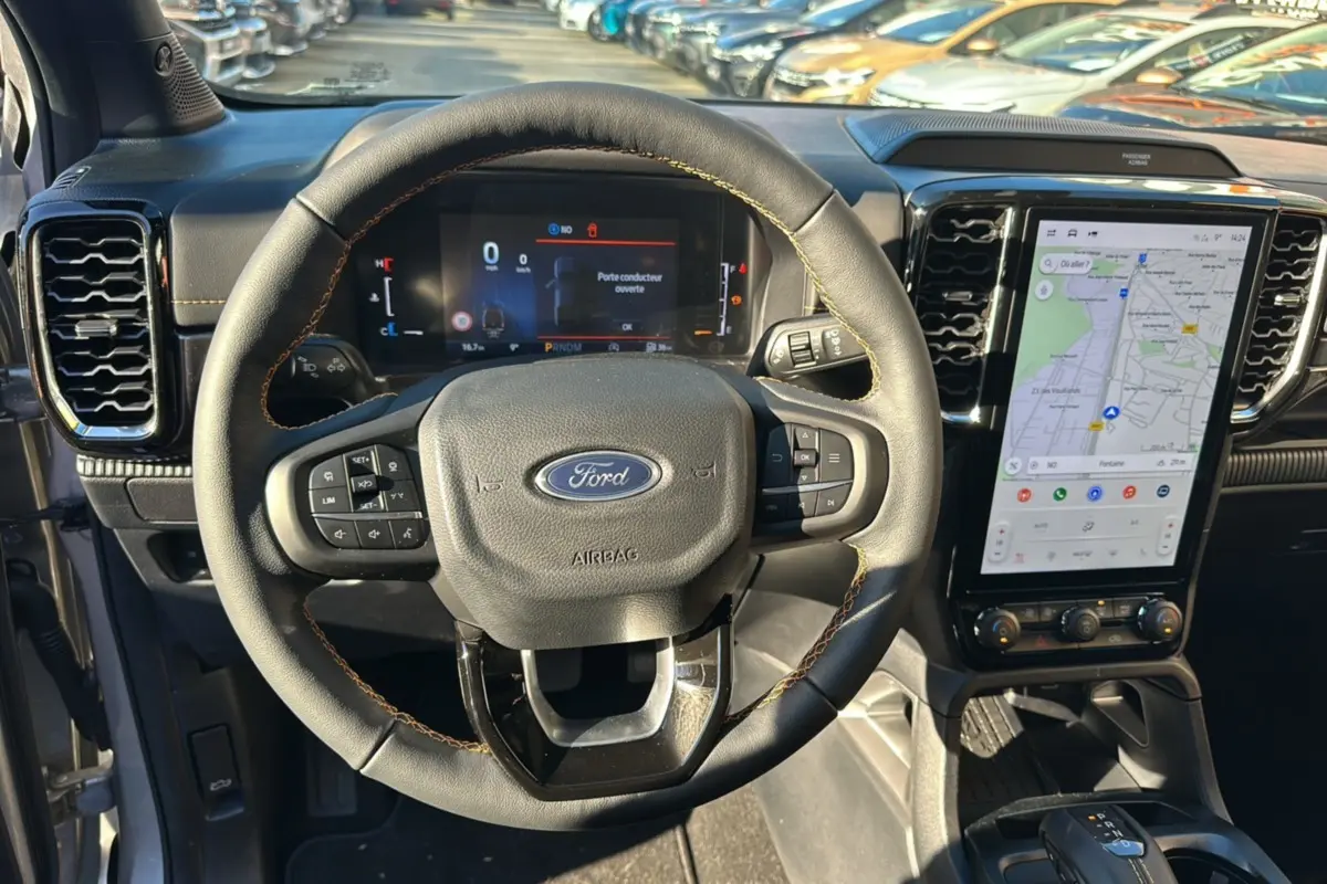 Vue intérieure centrée sur le volant du Ford Ranger 2025 gris iconic, avec écran tactile vertical et commandes au volant visibles.