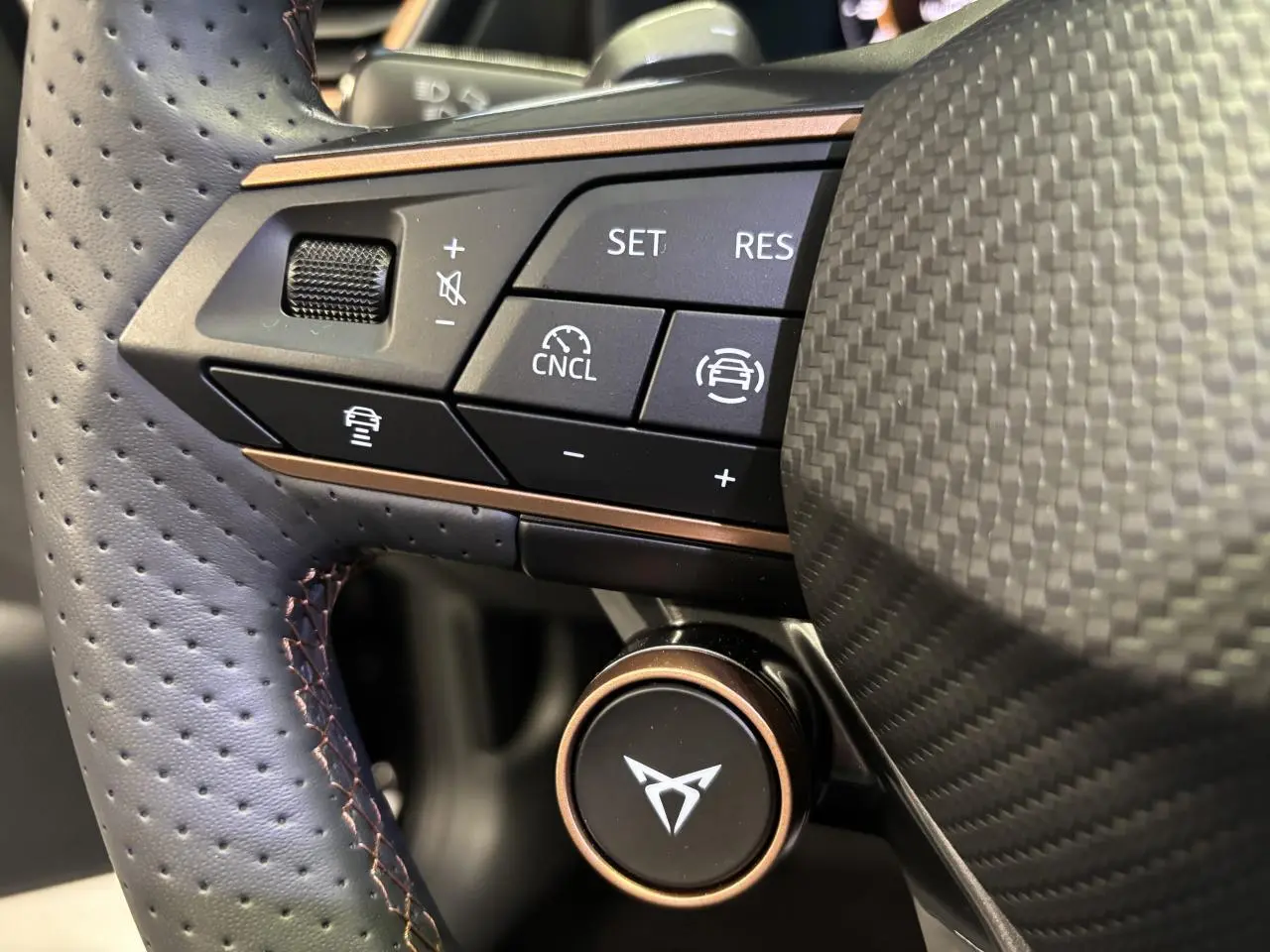 Gros plan sur le volant perforé noir avec surpiqûres cuivrées et commandes multifonctions du CUPRA Leon 2026.