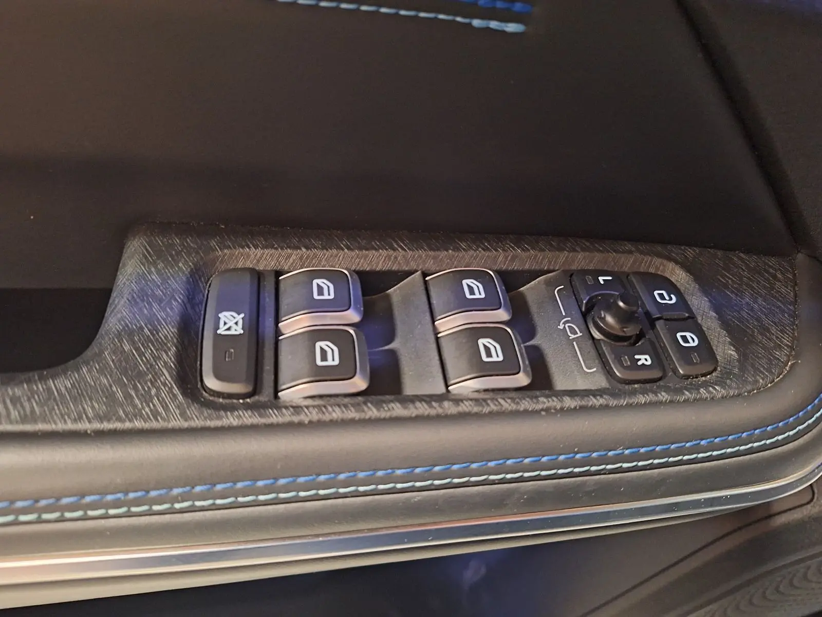 Gros plan sur les commandes de lève-vitres et rétroviseurs côté conducteur avec surpiqûres bleues sur porte noire.
