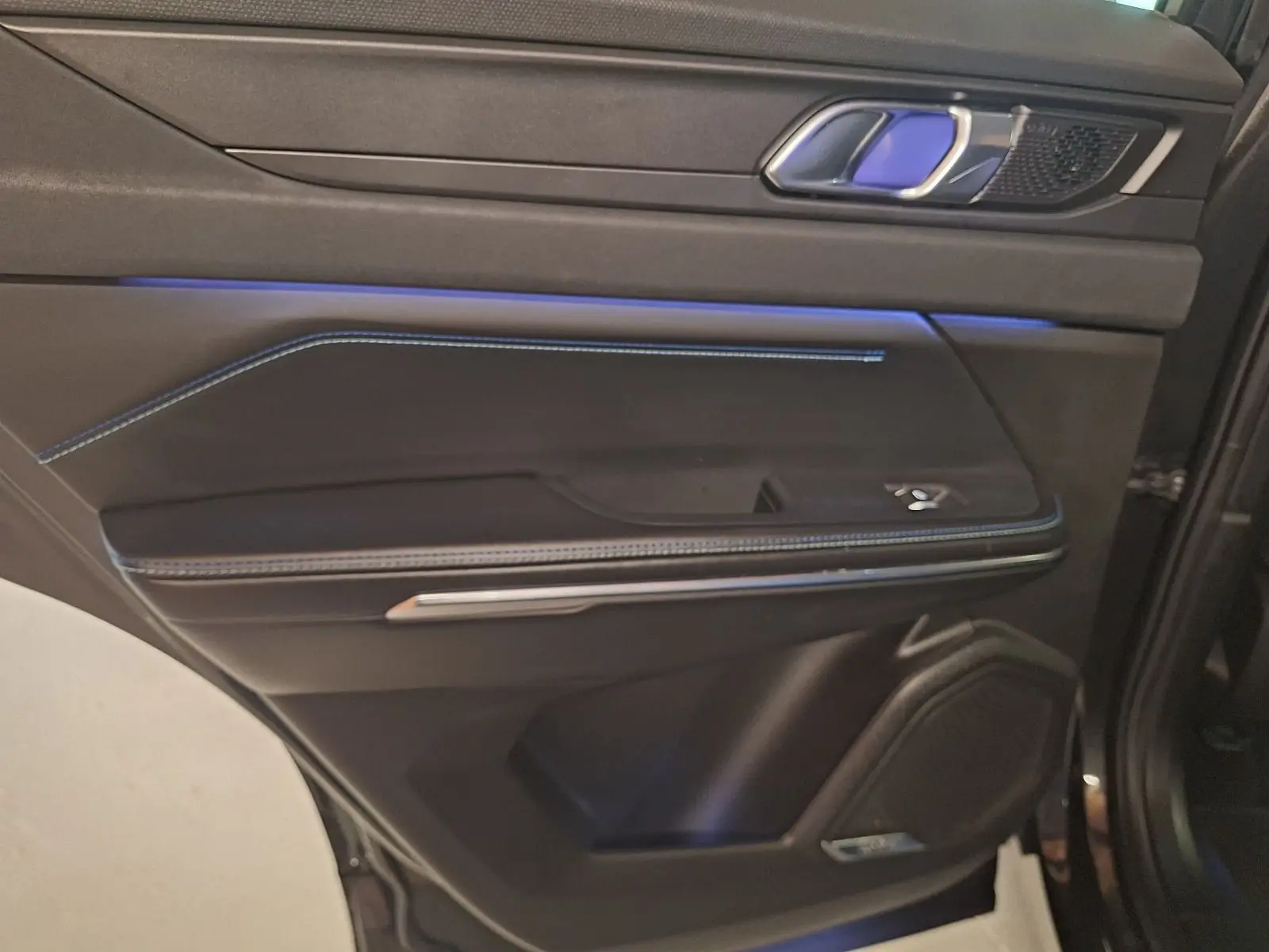 Gros plan sur la porte arrière droite noire du Lynk & Co 01 avec éclairage d’ambiance bleu et surpiqûres bleues.