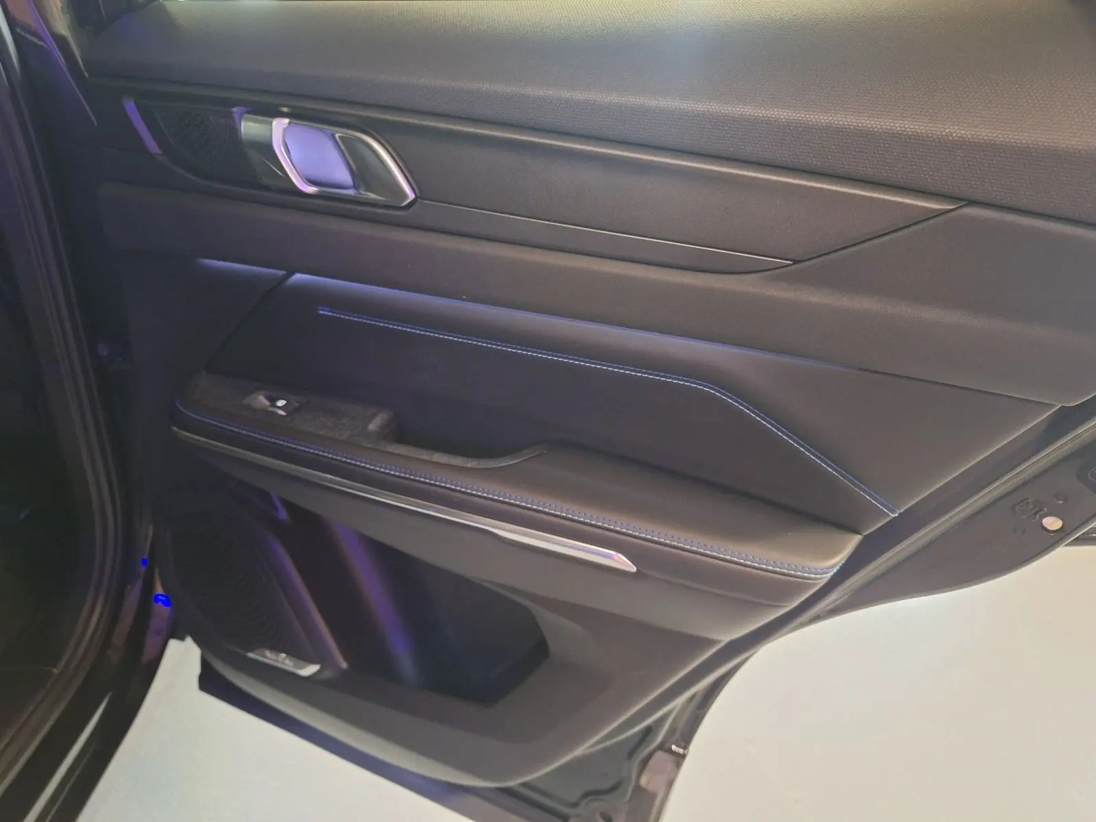 Gros plan sur la porte arrière droite noire du LYNK & CO 01 PHEV avec surpiqûres bleues et poignée chromée.