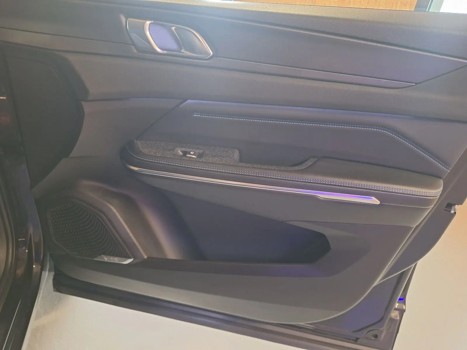 Vue intérieure du panneau de porte avant gauche noir du Lynk & Co 01 PHEV avec éclairage d'ambiance violet.