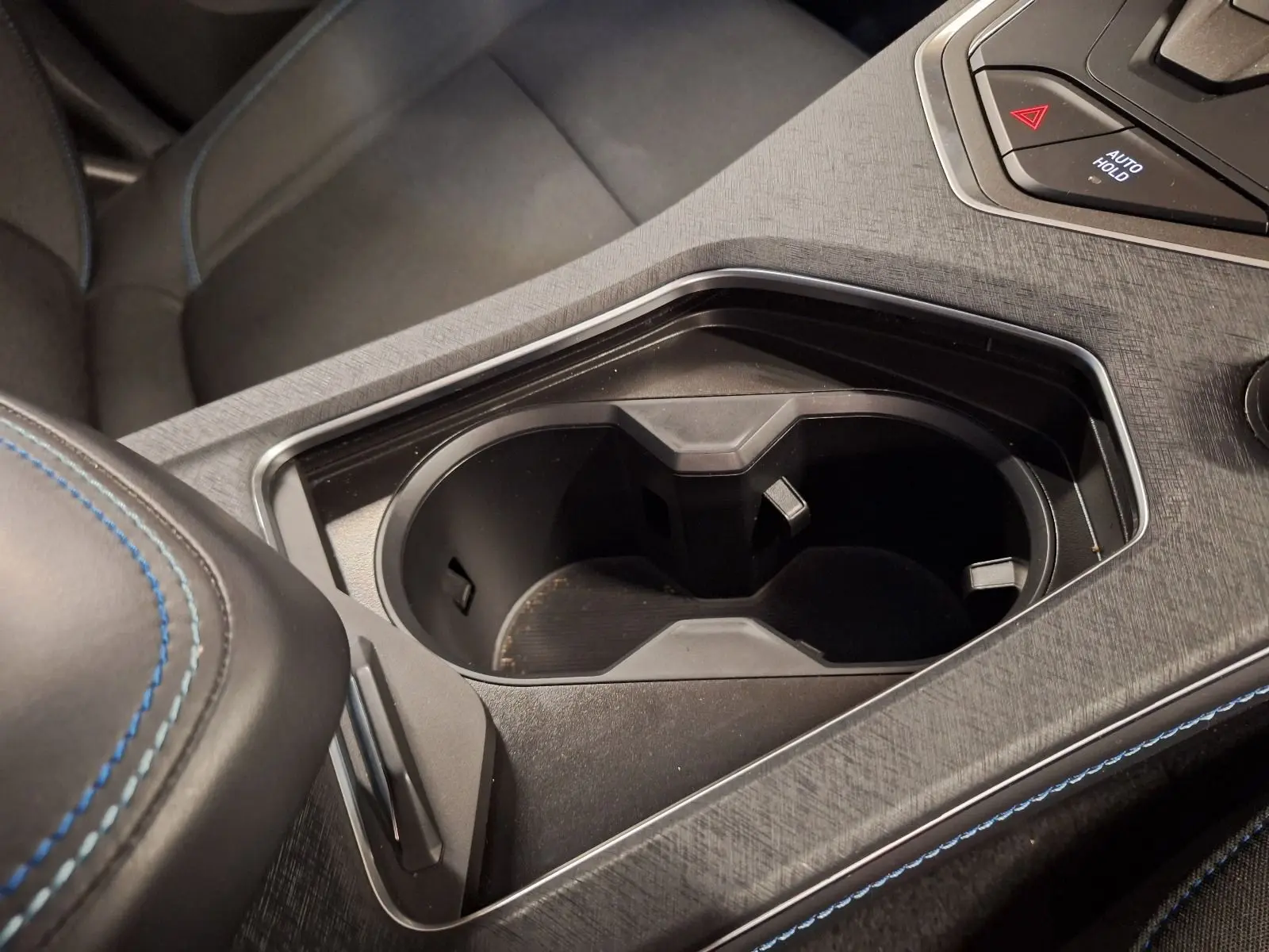 Gros plan sur le porte-gobelets noir et l'accoudoir central avec surpiqûres bleues dans l'habitacle du Lynk & Co 01 PHEV.