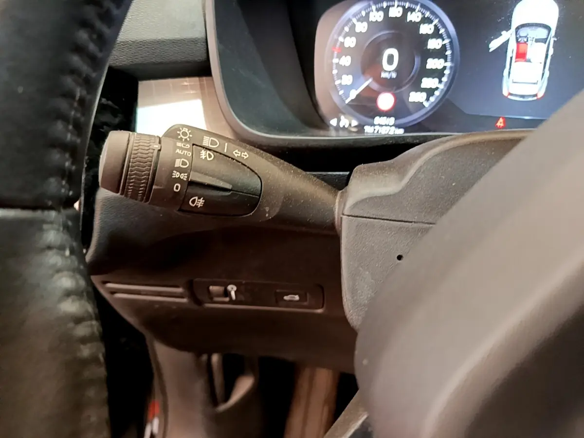 Gros plan sur le commodo d’éclairage à gauche du volant noir, avec tableau de bord digital du Volvo XC40 T2 2020 en arrière-plan.