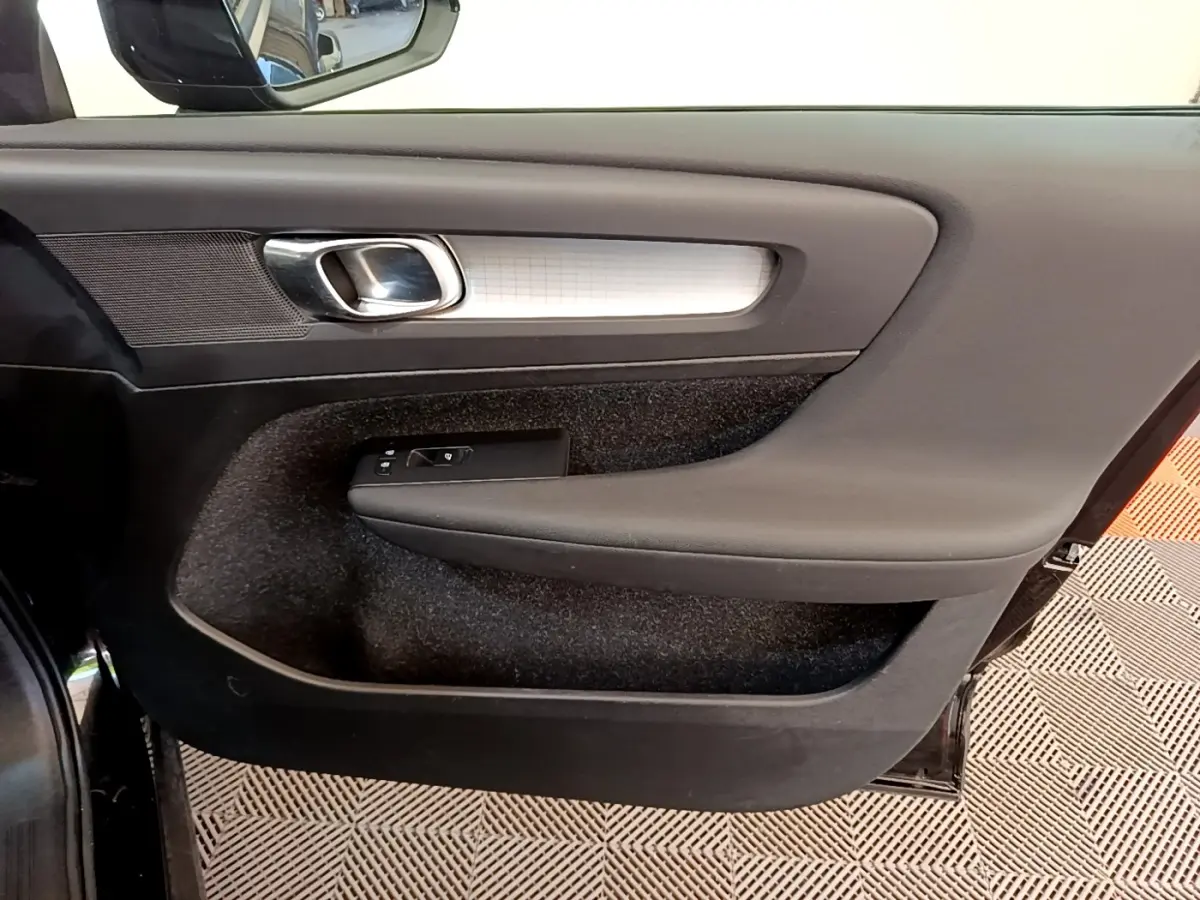 Vue rapprochée de la porte intérieure côté gauche du Volvo XC40 noir, avec poignée argentée et commandes de fenêtre.