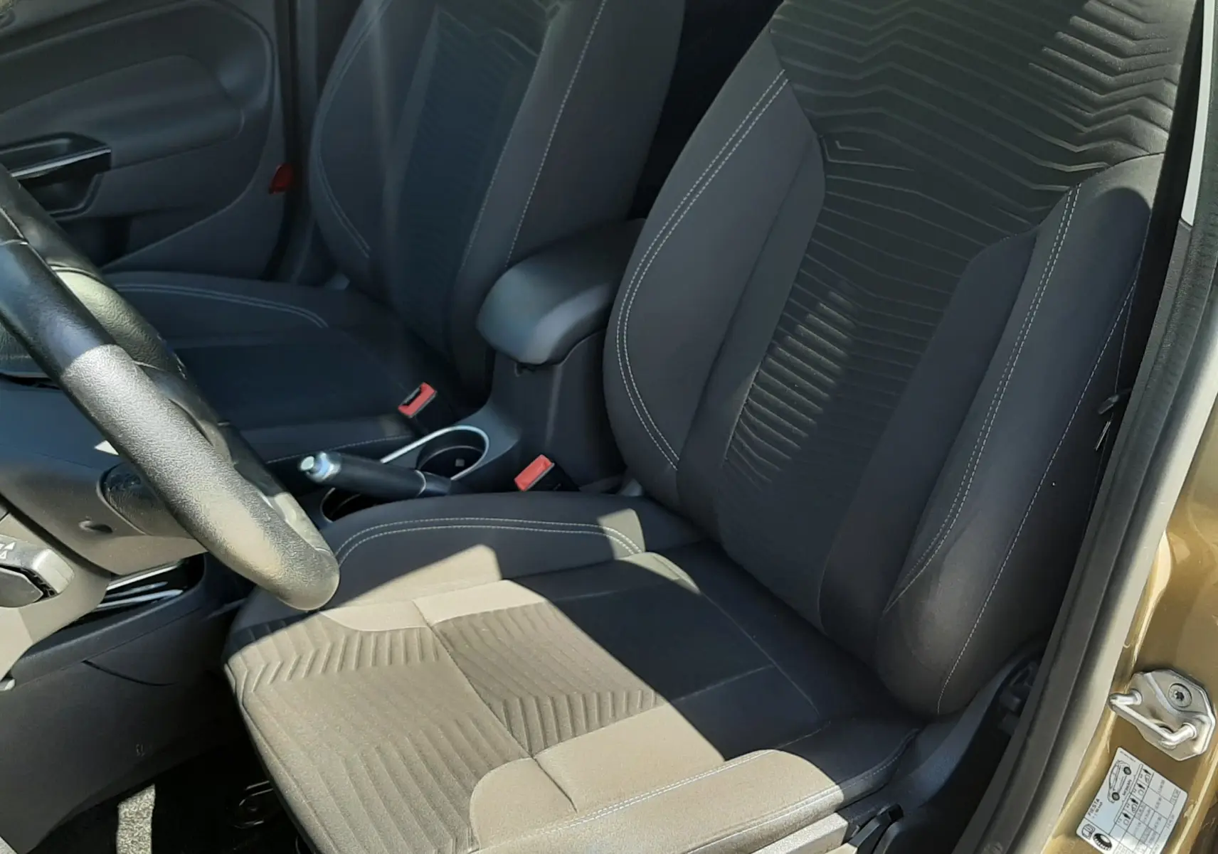 Vue intérieure côté conducteur de la Ford Fiesta 2013, sièges tissu noir avec motifs géométriques et volant visible.