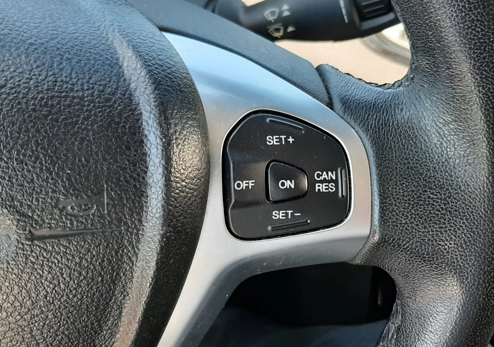 Gros plan sur les commandes de régulateur de vitesse au volant noir d'une Ford Fiesta marron métal de 2013.