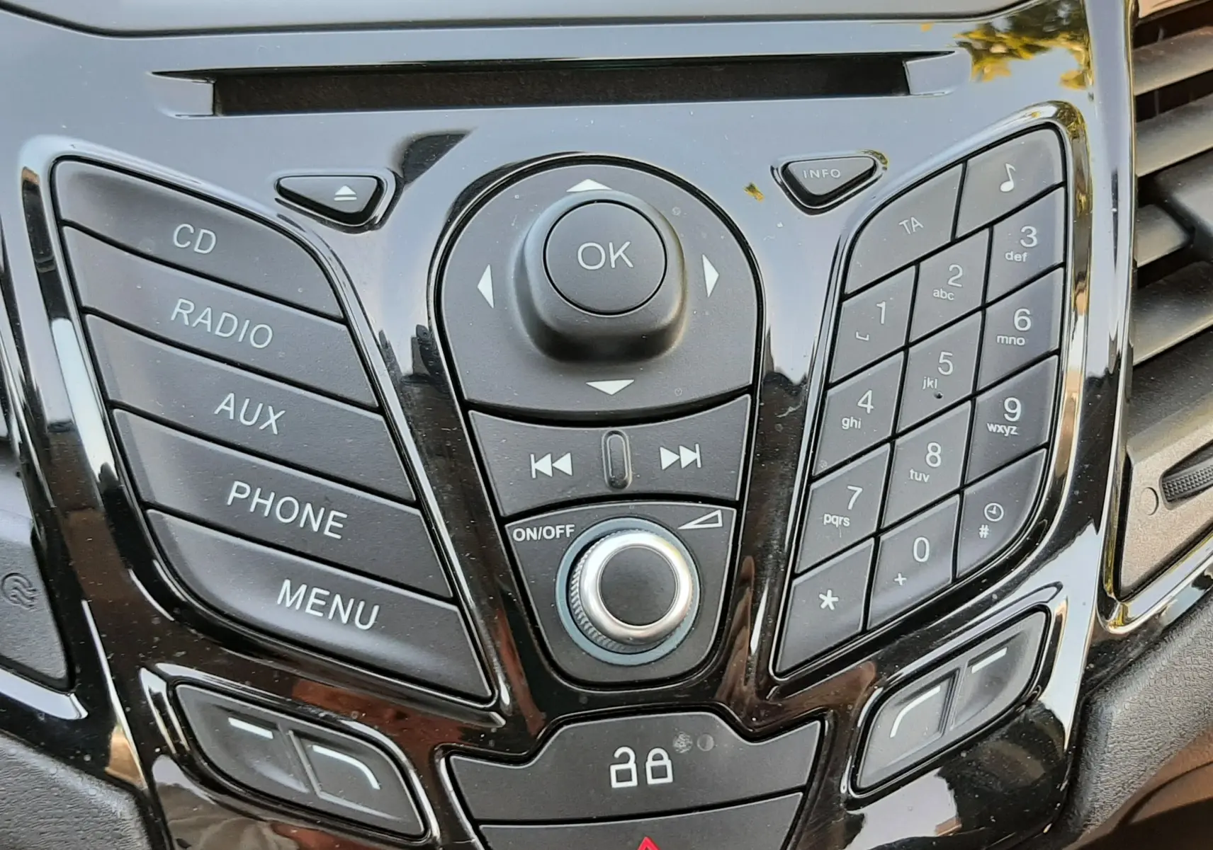 Vue rapprochée du tableau de bord noir brillant de la Ford Fiesta 2013, avec commandes audio et climatisation visibles.