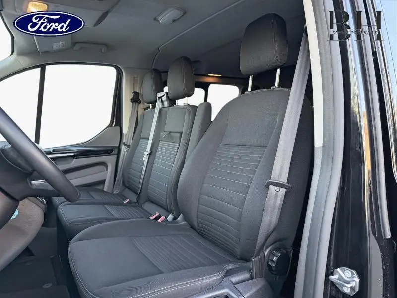 Vue intérieure côté conducteur du Ford Transit Custom Fourgon 2023 noir Agate, montrant les sièges avant en tissu noir.