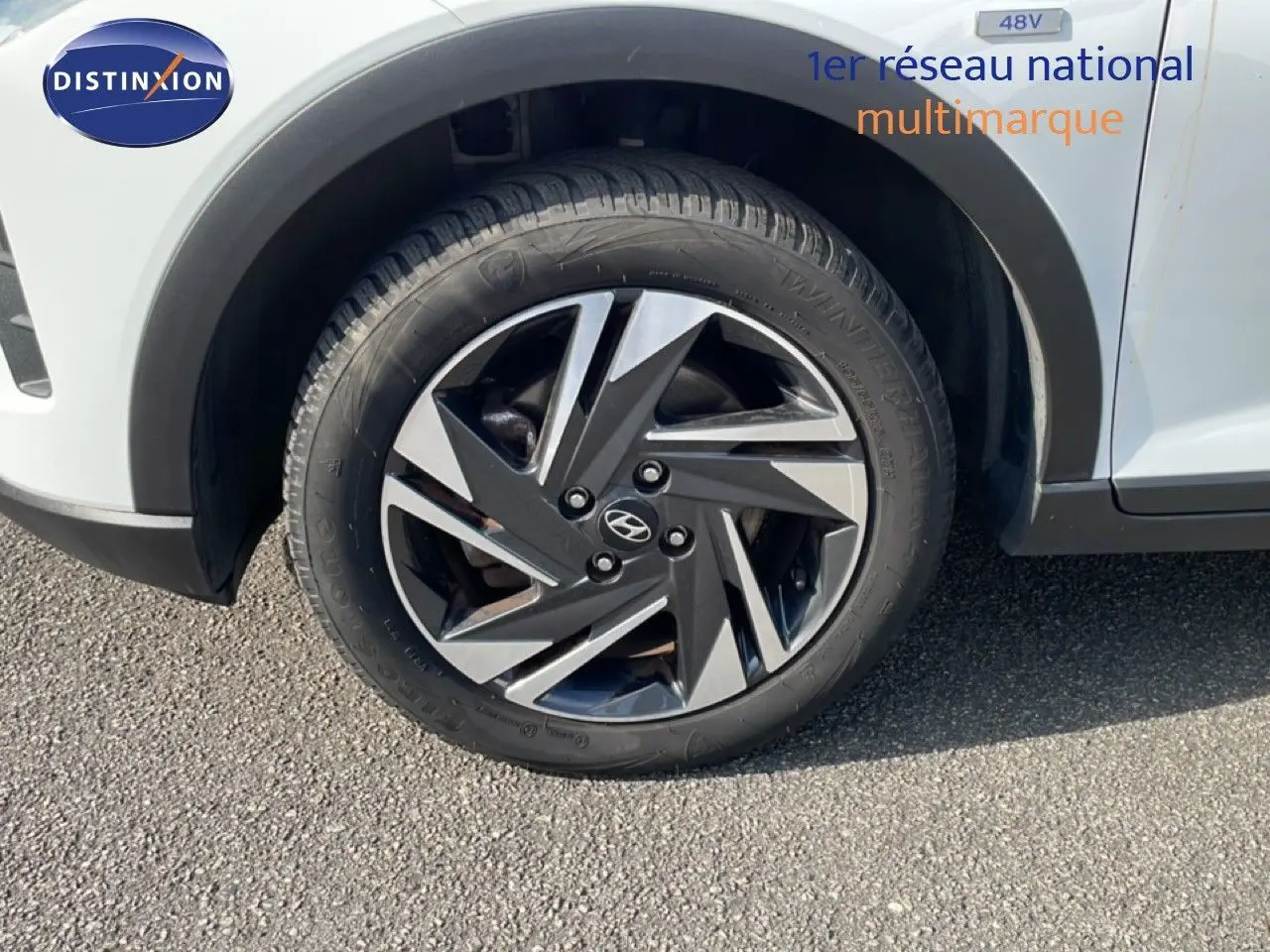 Gros plan sur la roue avant droite d’une Hyundai Bayon blanche polaire avec jante alliage bicolore et badge Hyundai.